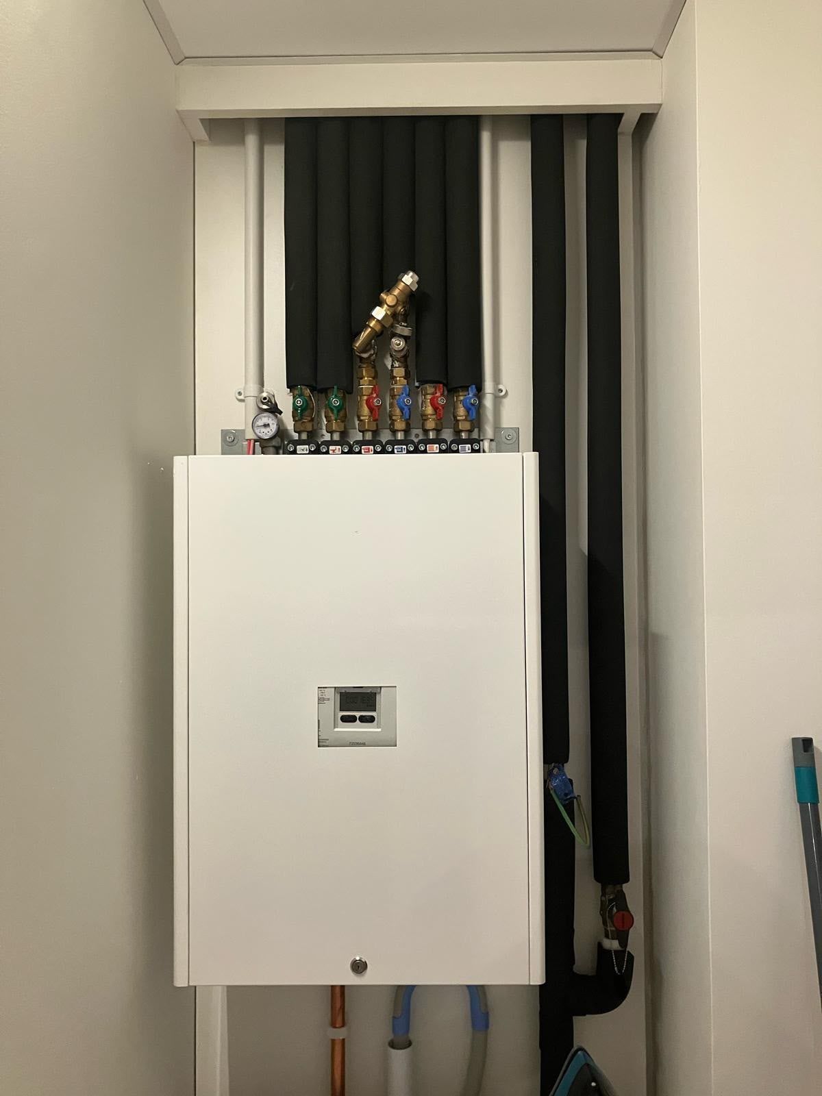 Heat interface unit fitted in a white utility cupboard with insulated pipes